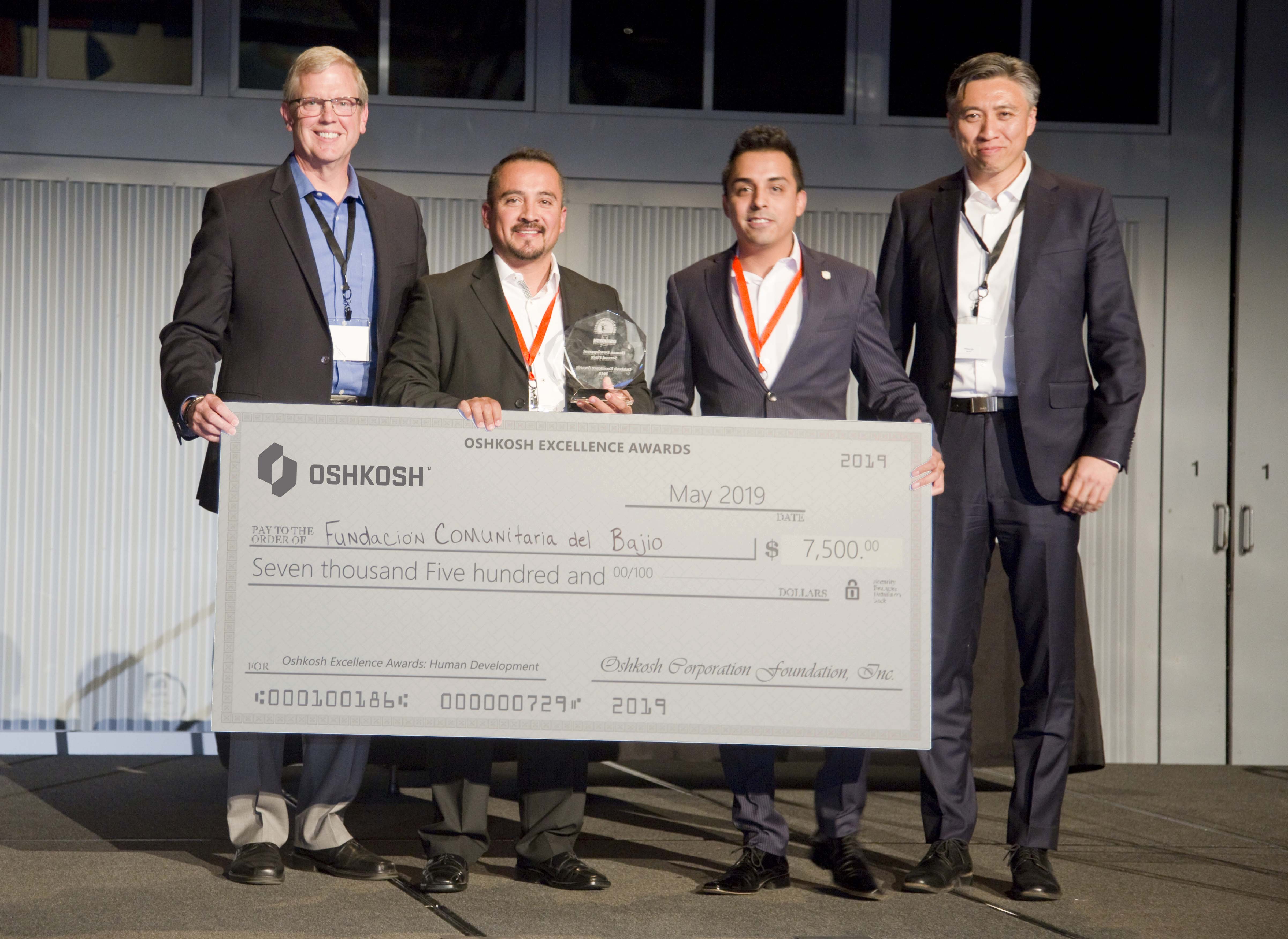 Four men in blue and black suits holding trophy and charity check for $7,500 at OEA global award ceremony 