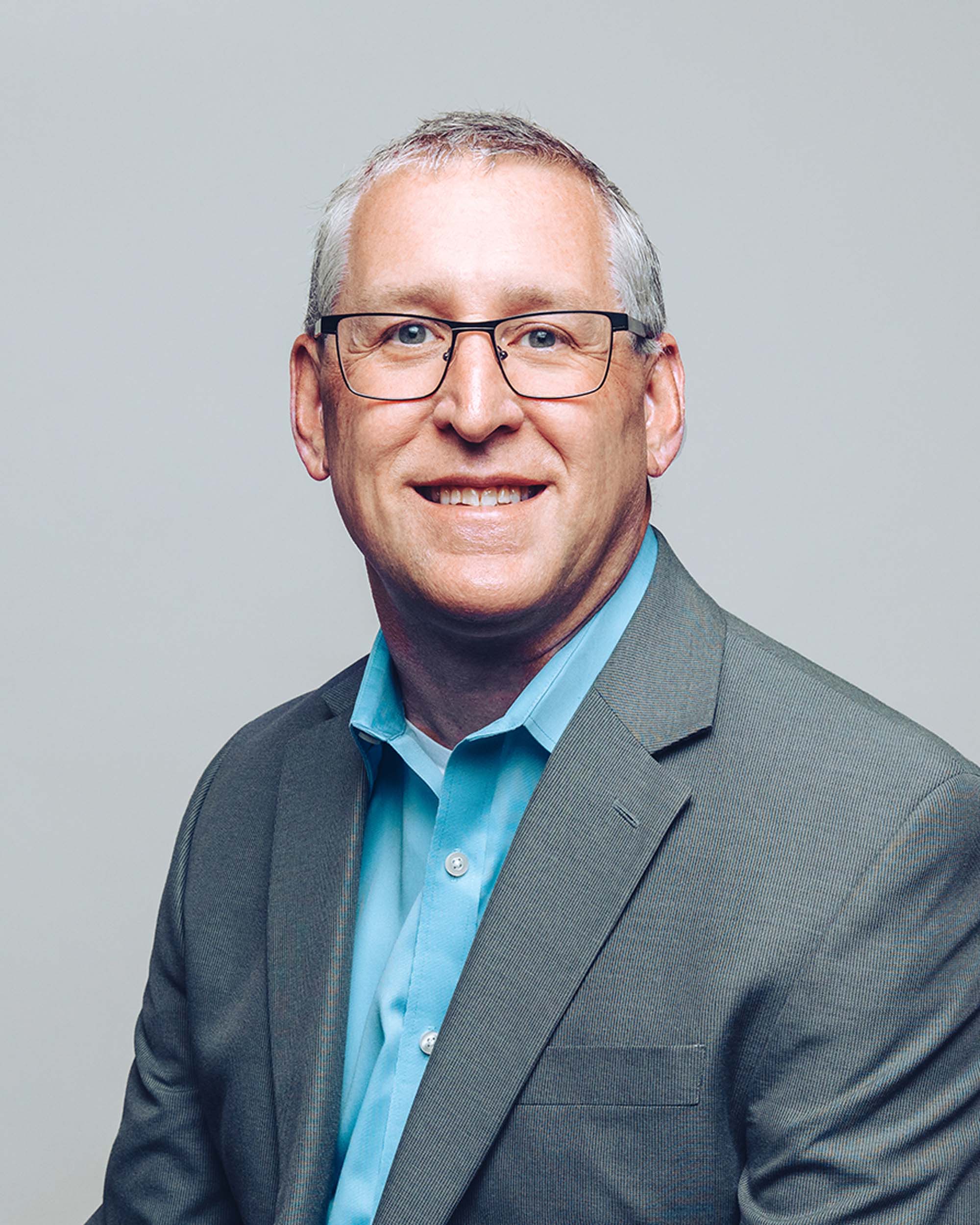 'Chris Freeders smiling and wearing a grey suit jacket on top of a light blue shirt'