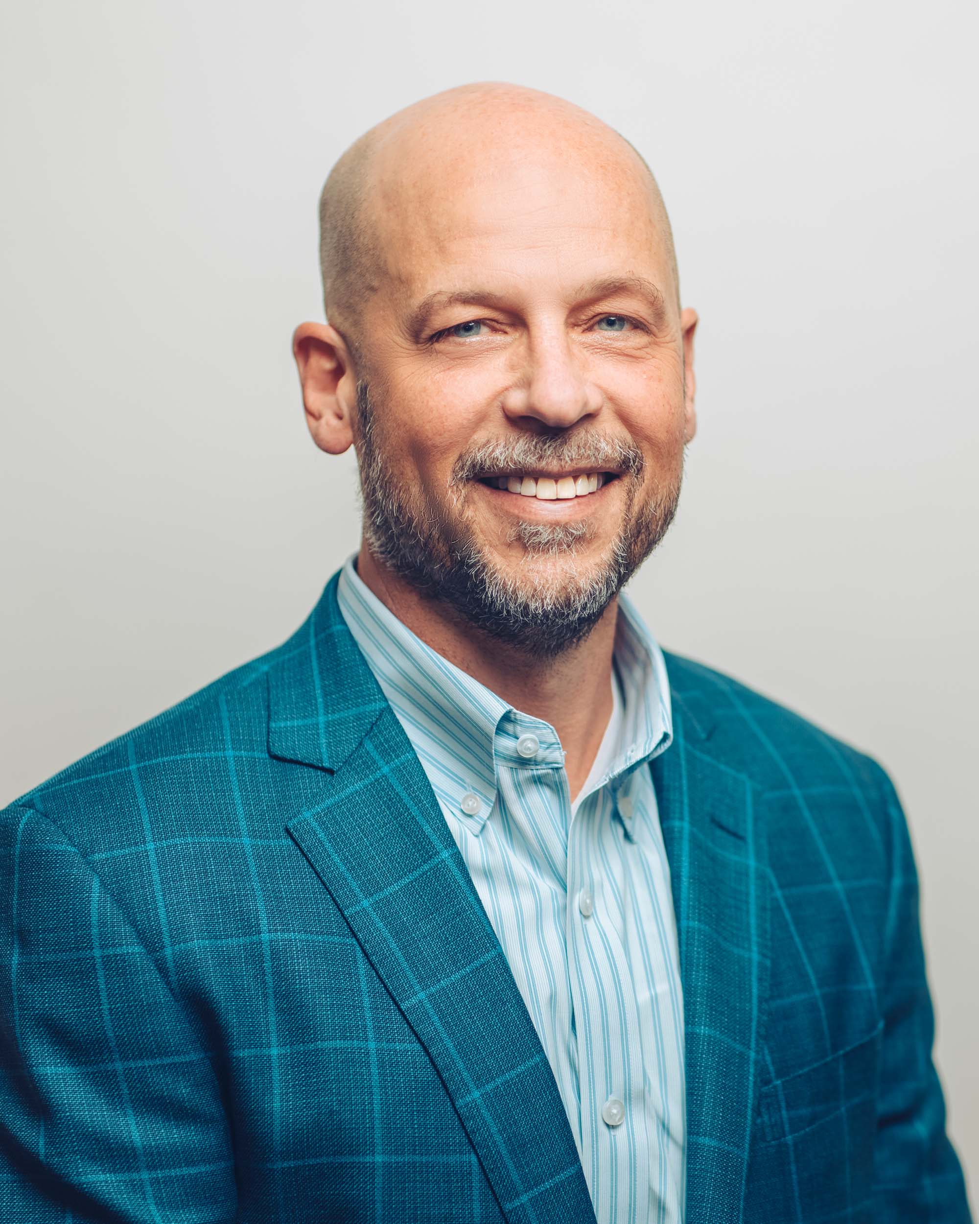 'John Pfeifer wearing a blue patterned suit coat smiling'