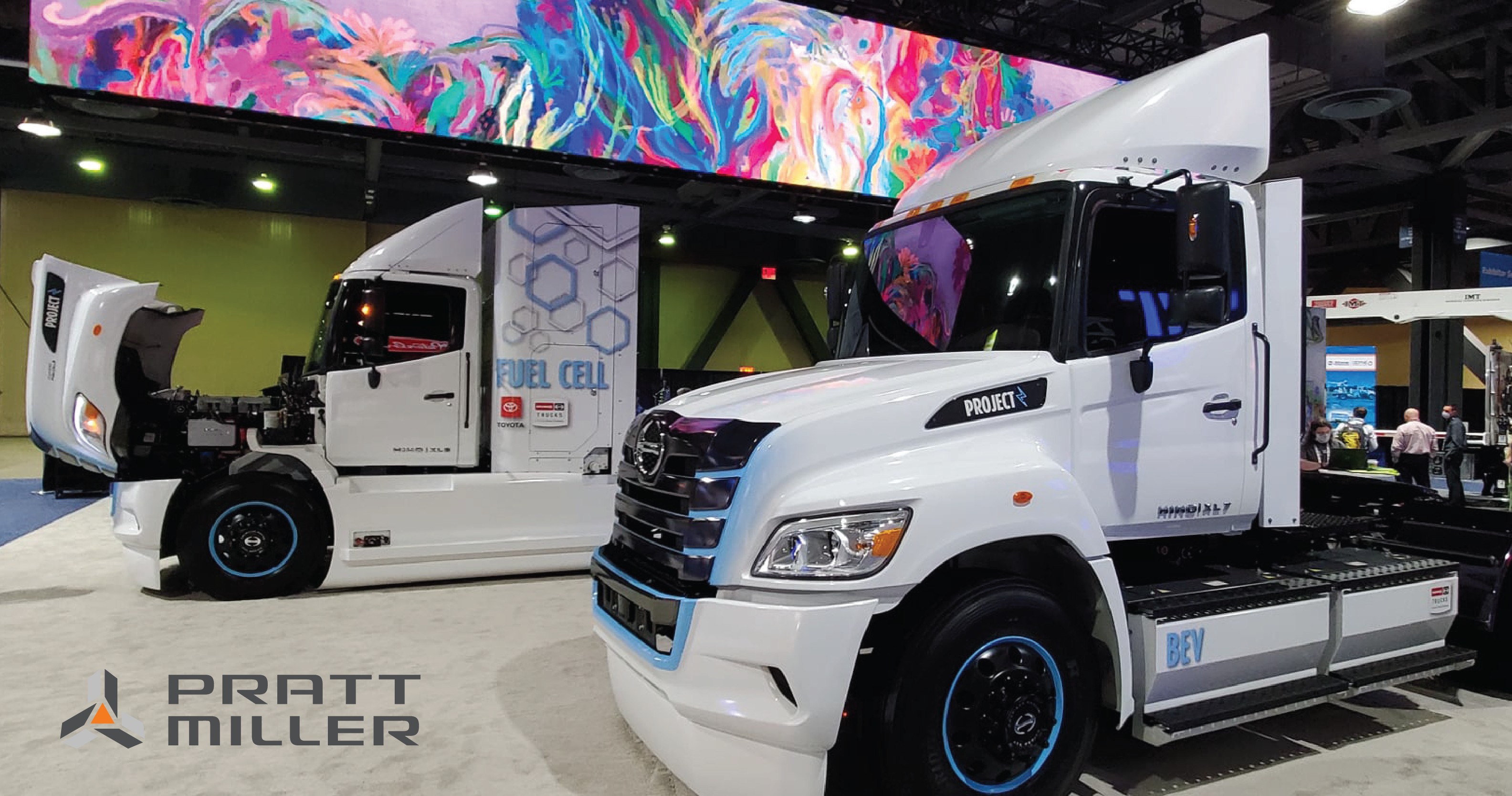 Pratt Miller logo with white electric semi-trucks inside a convention center