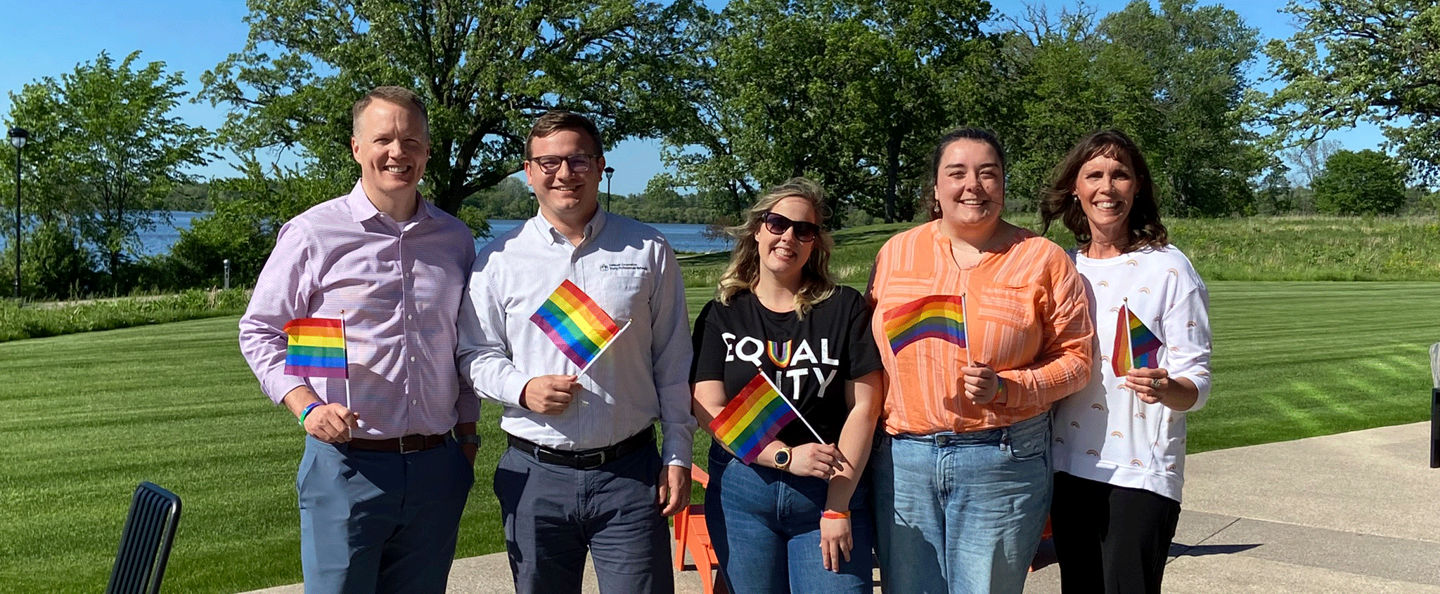 Oshkosh team members standing outside on a sunny day holding pride flags